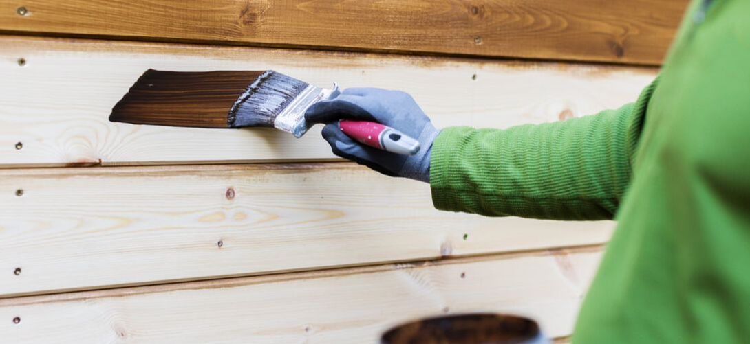 Painter applying stain to wood siding